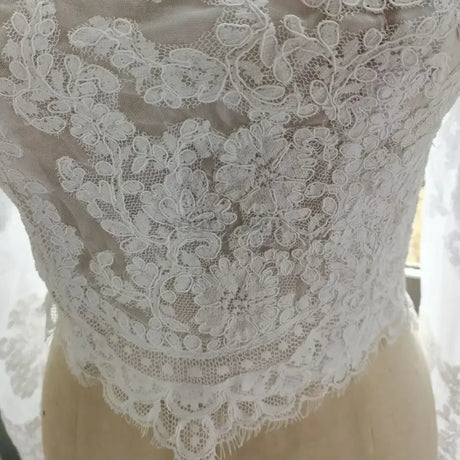 Close-up of intricate lace detailing on a white off-shoulder bridal jacket, highlighting floral appliqué design.