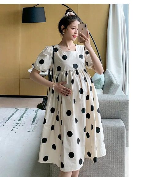 Model wearing a polka dot loose maternity dress in a bright indoor setting, showcasing a comfortable and stylish summer outfit.