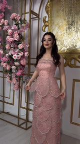 Model wearing a pink beaded engagement gown with tiered skirt, lace-up back, and floral backdrop.