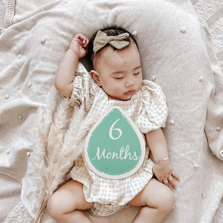Baby milestone photo showcasing a 6-month-old wearing a cute outfit with a bow, surrounded by soft textures.