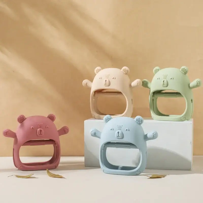 Colorful baby teether gloves in bear designs, made of soft silicone for infants, available in pink, beige, green, and blue.