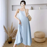 Pleated light blue maternity dress with adjustable straps, perfect for summer wear, styled in a modern indoor setting.