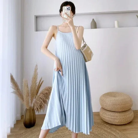 Pleated light blue maternity dress with adjustable straps, perfect for summer wear, styled in a modern indoor setting.