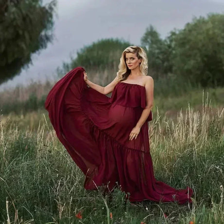 Pregnant woman in a burgundy boho two-piece maternity set, posing gracefully in a natural landscape.