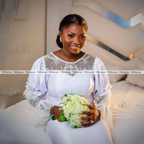 Smiling bride in a customized white wedding dress, holding a bouquet, showcasing elegant lace and beaded details.
