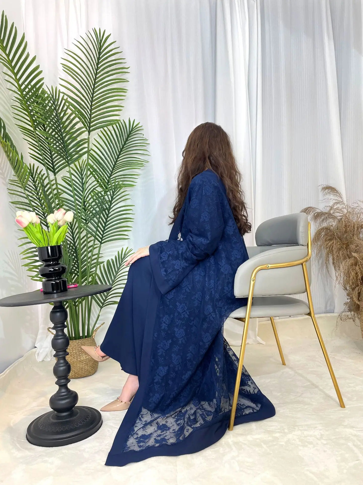 Elegant woman in a navy blue Dubai Moroccan Kaftan, featuring intricate lace details, seated in a stylish indoor setting.
