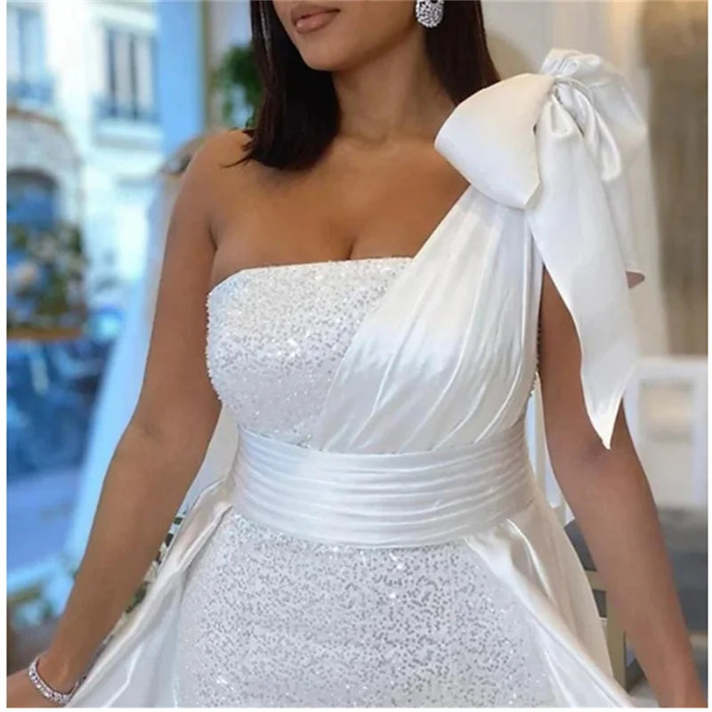 Elegant one-shoulder wedding dress with sequins and bow detail, perfect for modern brides.
