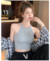 Young woman wearing a gray knitted tank top, styled casually with a plaid shirt and relaxed pants.