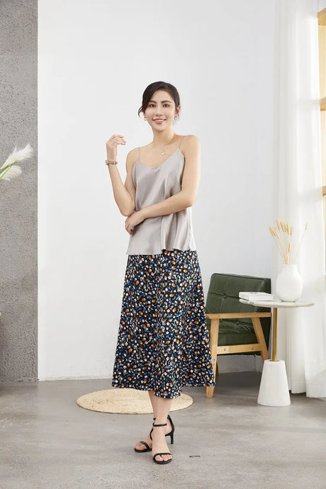 Model wearing a sleek silver satin camisole with a floral skirt, showcasing summer fashion style in a modern setting.