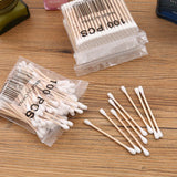 100pcs bag of baby cotton swabs on a wooden surface, showcasing the cotton ends and wooden sticks.