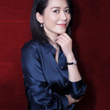 Model wearing a satin long sleeve silk shirt, posing with a smile and elegant accessories against a red background.