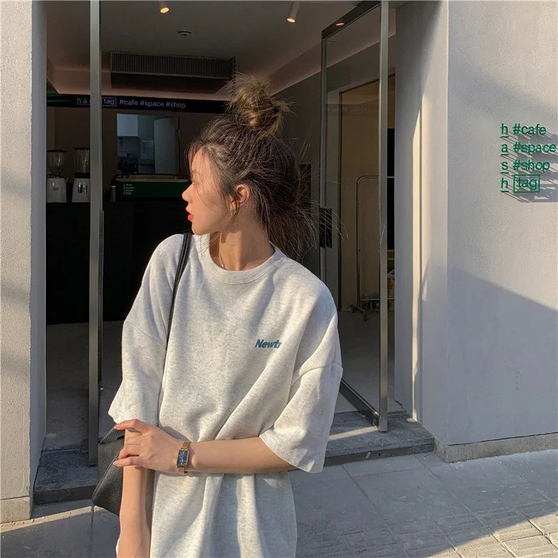 A young woman wearing an oversized gray Harajuku streetwear tee, posing casually outside a cafe.