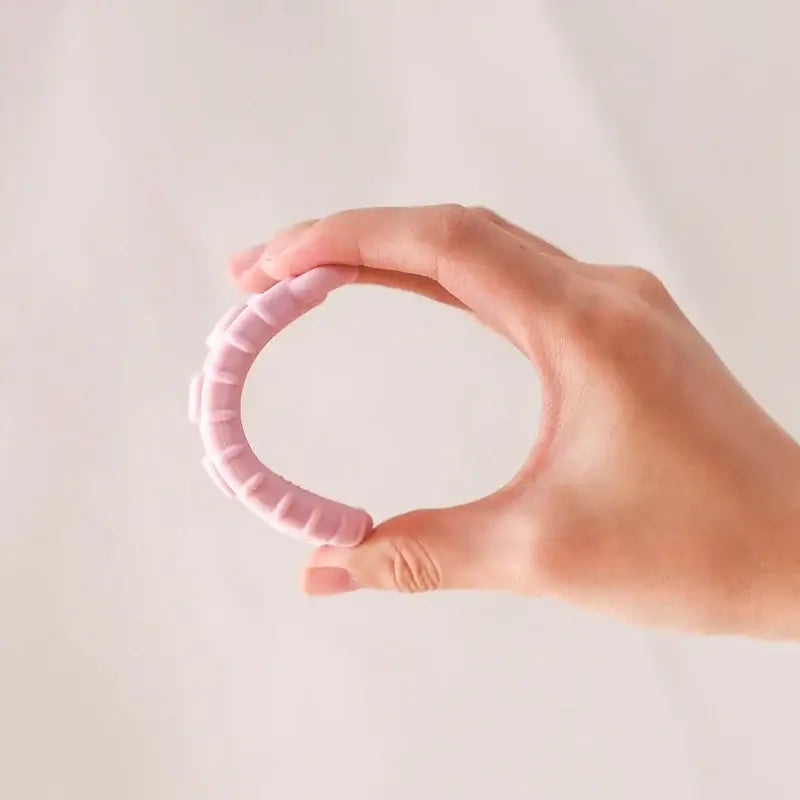 Hand holding a soft pink baby teether glove made of safe silicone material for infants.