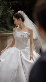 Elegant off-shoulder bridal gown featuring a voluminous satin skirt and delicate veil, perfect for weddings.