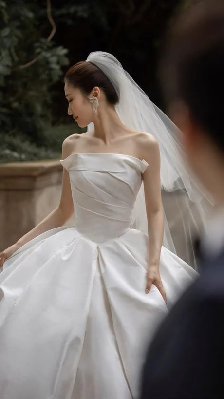 Elegant off-shoulder bridal gown featuring a voluminous satin skirt and delicate veil, perfect for weddings.