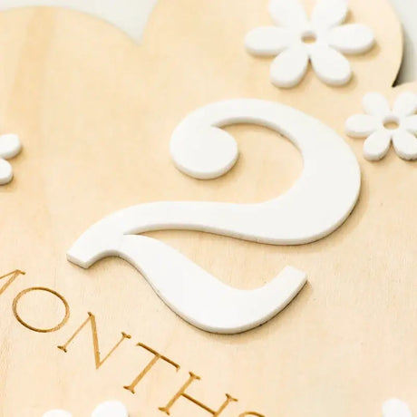 Close-up of a wooden milestone marker with the number 2 and decorative flowers, for tracking baby’s age in months.