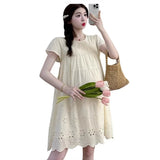 Woman wearing a knee-length A-line cotton maternity dress in cream, holding flowers and a handbag, perfect for summer.
