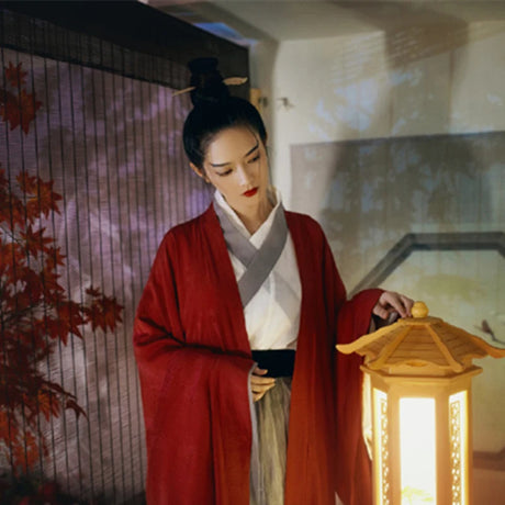 A woman in a wine red Swordsman Hanfu costume from the Tang Dynasty, illuminating a lantern in a serene setting.