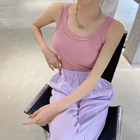 Model wearing a pink ribbed tank top with a casual style, paired with lilac pants, showcasing modern streetwear fashion.