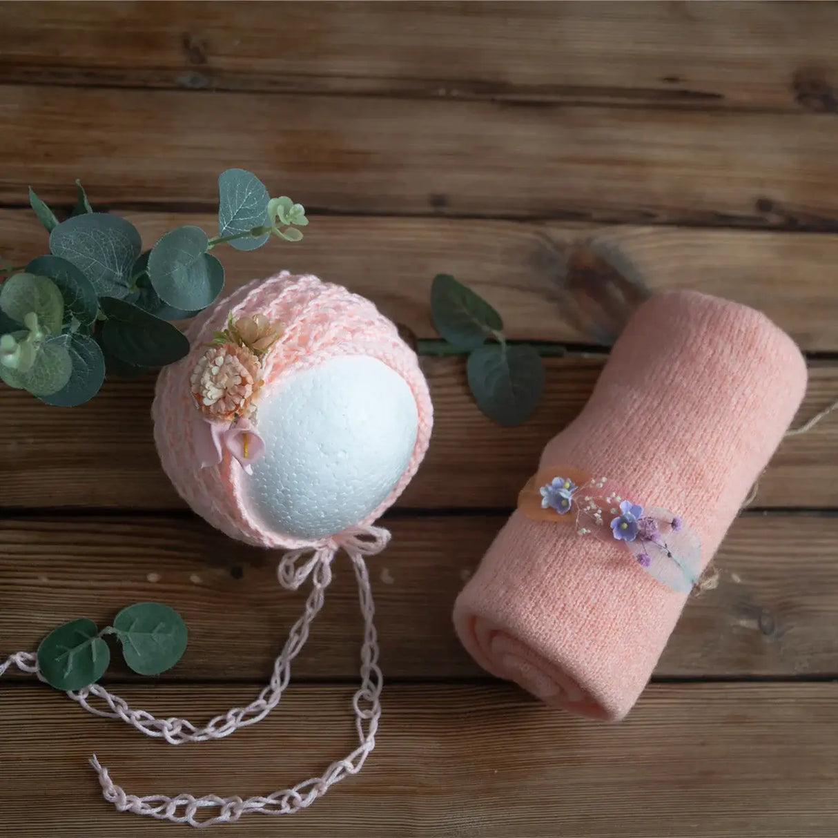 Newborn stretch knit mohair set featuring soft coral wrap and decorative floral bonnet on wooden background.