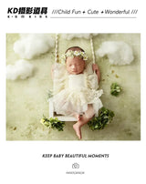 Baby girl in a floral headband swinging in a cloud-themed nursery for newborn photography.