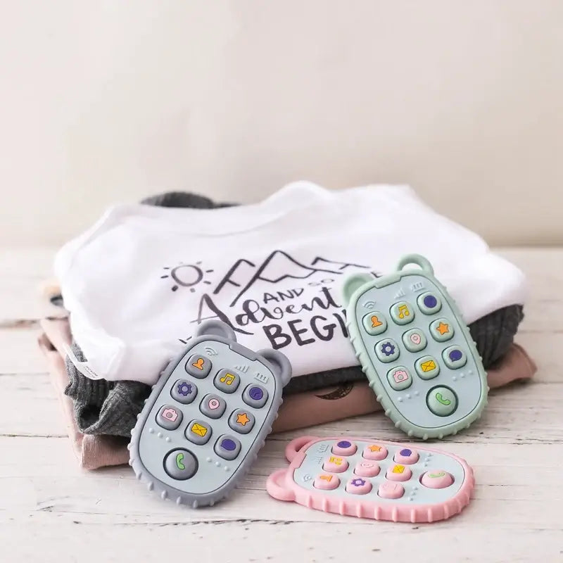 Soft baby remote controls in pastel colors beside cute baby clothes, designed for early development and play.