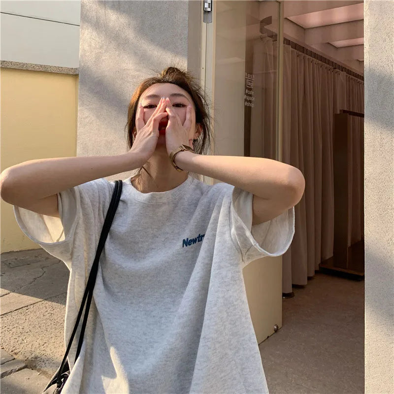 Woman wearing an oversized gray Harajuku streetwear tee, styled casually in an urban setting.