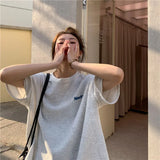 Woman wearing an oversized gray Harajuku streetwear tee, styled casually in an urban setting.