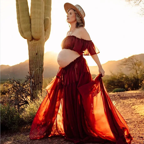 Pregnant woman in a boho two-piece maternity set at sunset, wearing a straw hat, surrounded by desert scenery.