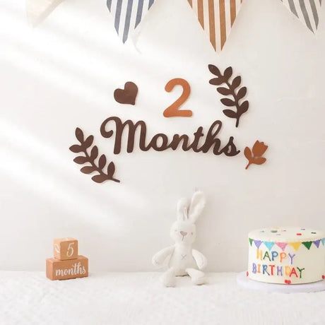 2 Months milestone card display with soft felt leaves, blocks, a bunny toy, and a festive cake backdrop.
