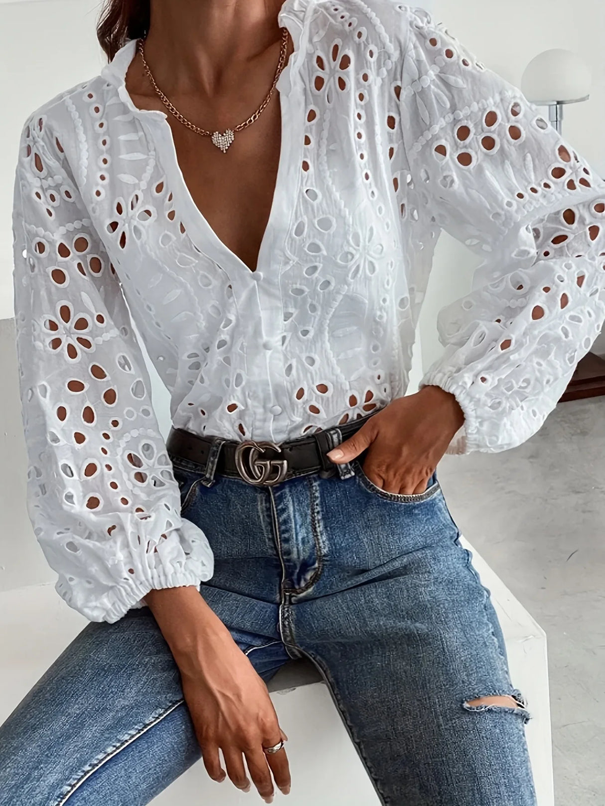 Elegant women's Hollow Out White Lace Shirt with long sleeves styled with a belt and jeans.