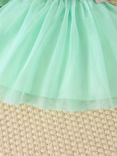 Mint green tulle skirt of a newborn baby girl dress laying on a textured beige surface.