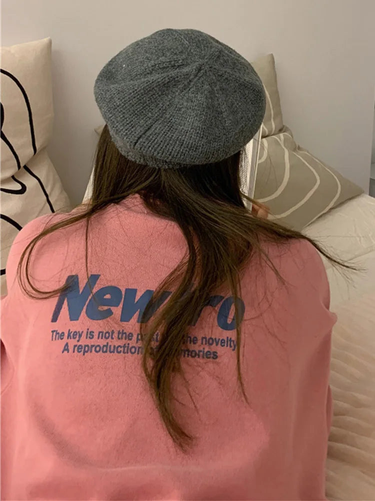 Back view of a young woman wearing a pink sweatshirt with 'Newero' print and a grey beret.