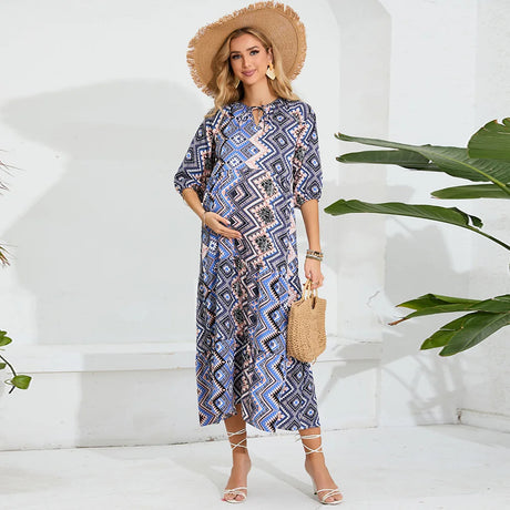 Elegant beach maternity dress in geometric pattern, perfect for summer photoshoots, styled with a straw hat and handbag.