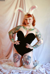 Woman in a black velvet strapless bodysuit with bunny ears, showcasing vibrant tattoos and a playful pose.