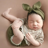Newborn baby peacefully sleeping in a cotton outfit with a bow headband, perfect for photography props.