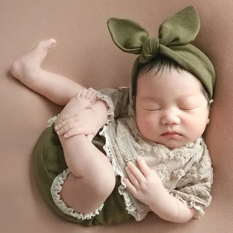 Newborn baby peacefully sleeping in a cotton outfit with a bow headband, perfect for photography props.