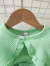 Close-up of a mint green baby dress with textured fabric and button closure hanging on a wooden hanger.