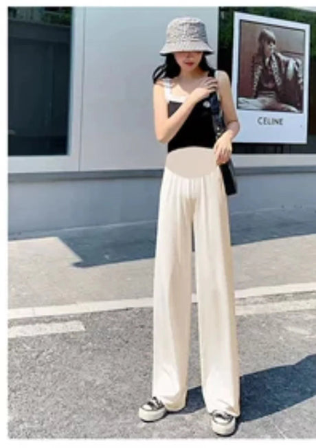 Stylish woman wearing ice silk pleated maternity pants, paired with a black top and hat, in a summer setting.