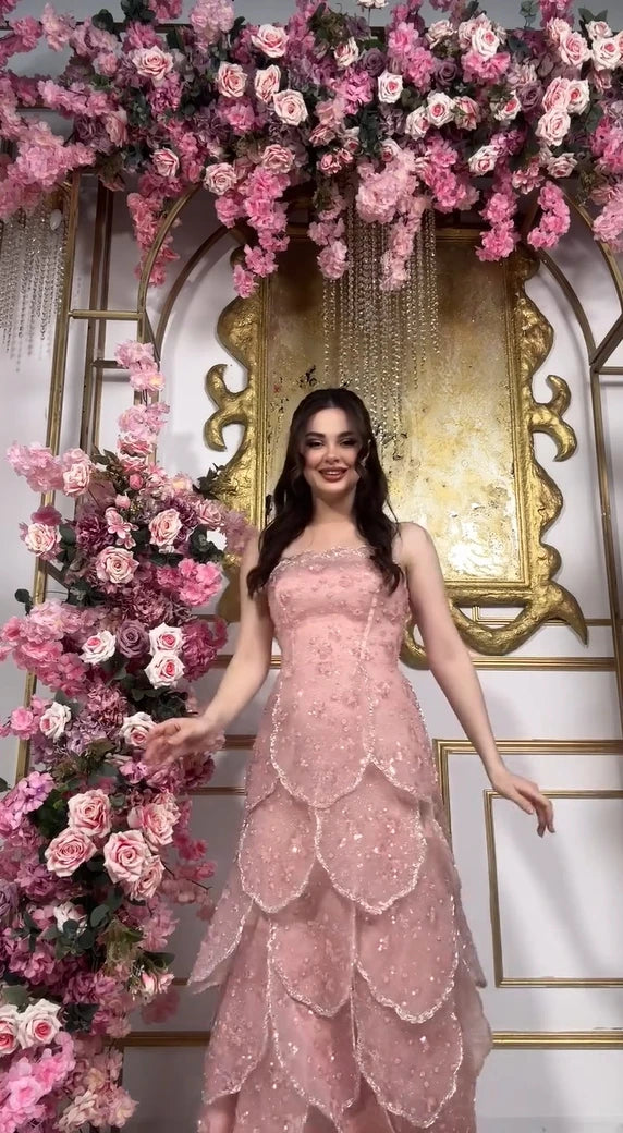 Pink beaded engagement gown with tiered skirt, model surrounded by floral decorations.