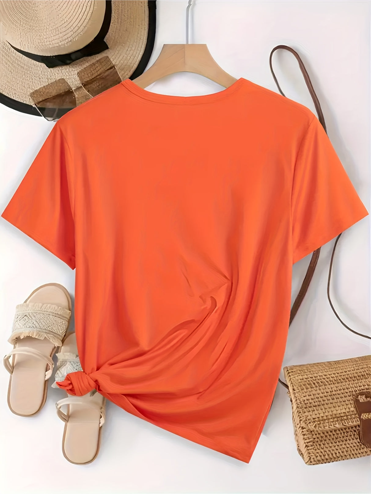 Back view of an elegant orange all-season round neck t-shirt styled with sandals and a straw hat.